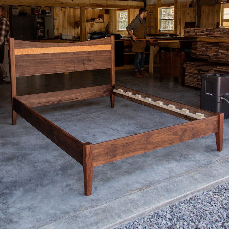 May include: A wooden bed frame with a walnut headboard and a slatted base. The headboard has a curved top and a thin strip of maple veneer.