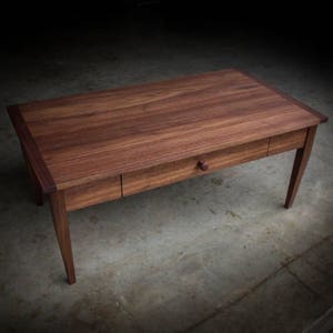 May include: A dark brown wooden coffee table with a single drawer and a wooden knob. The table has a rectangular top and four legs.