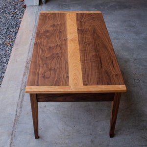 May include: A rectangular coffee table with a walnut wood top and a cherry wood inlay. The table has a simple design with four legs and a drawer.