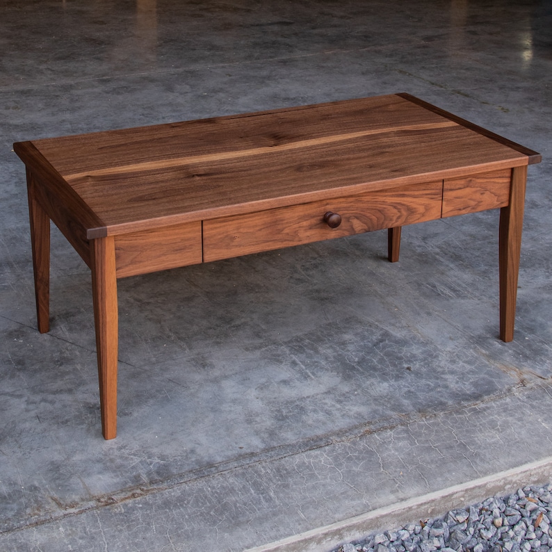 May include: A dark brown wooden coffee table with a single drawer and a rounded knob. The table has a simple, rectangular design with straight legs.