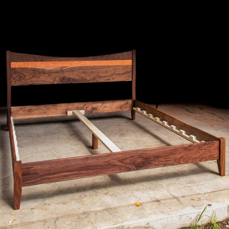 May include: A wooden bed frame with a walnut finish. The headboard has a curved top and a thin strip of maple veneer. The frame has a slatted base.