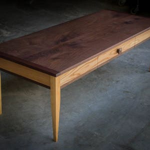 May include: A wooden desk with a walnut top and a drawer. The desk has a light wood base and legs.