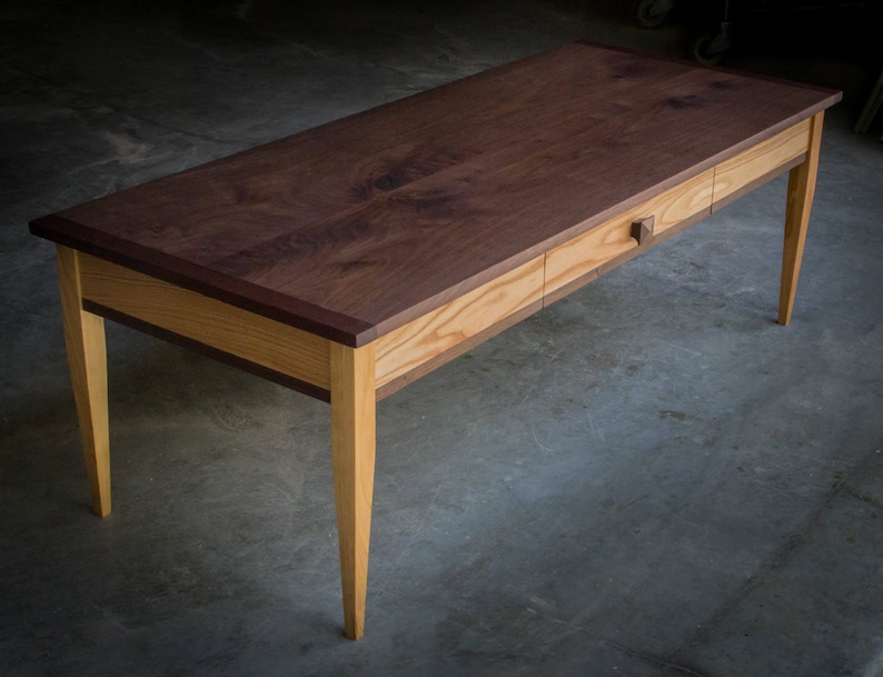 May include: A wooden desk with a walnut top and a drawer. The desk has a light wood base and legs.
