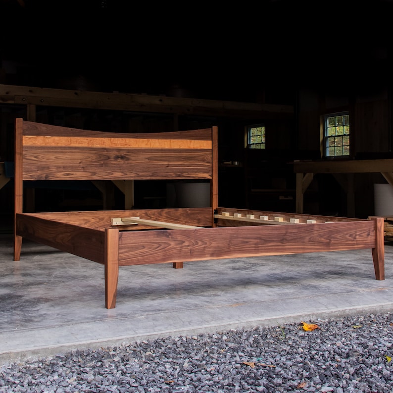 May include: A wooden bed frame with a curved headboard and a walnut finish. The bed frame has a simple design with straight legs and a slatted base.