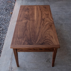 May include: A dark brown wooden coffee table with a rectangular top and four legs. The table has a natural wood grain pattern.