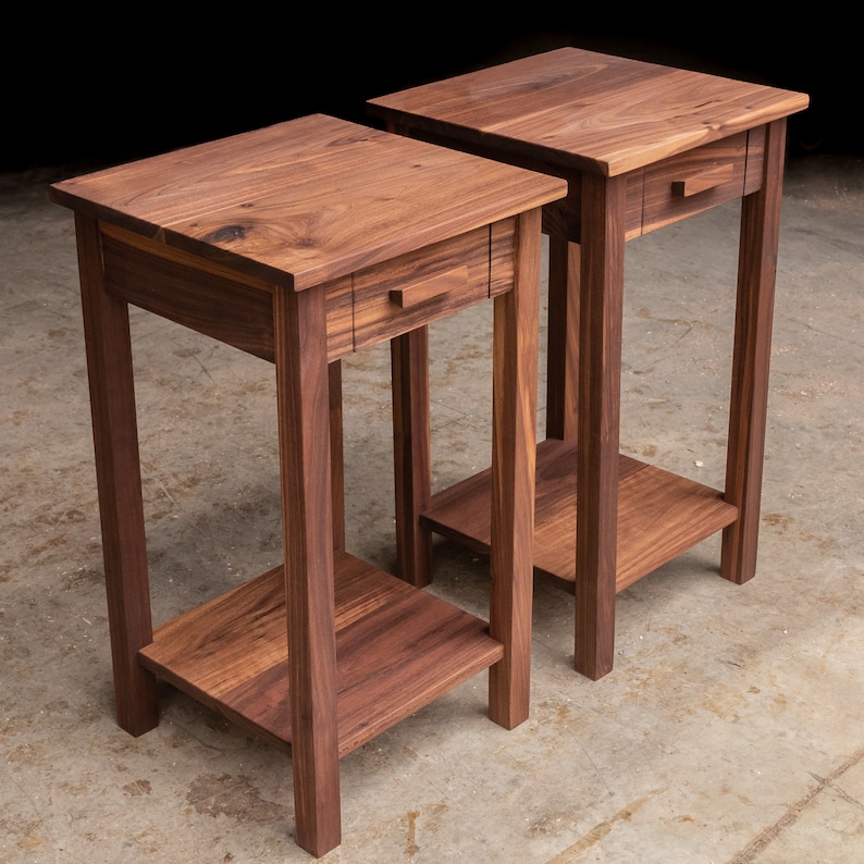 May include: Two matching wooden end tables with a drawer and a lower shelf. The tables are made of dark walnut wood and have a simple, modern design.