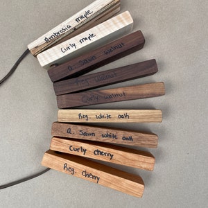 May include: A collection of wood samples labeled with different types of wood, including ambrosia maple, curly maple, walnut, white oak, and cherry.