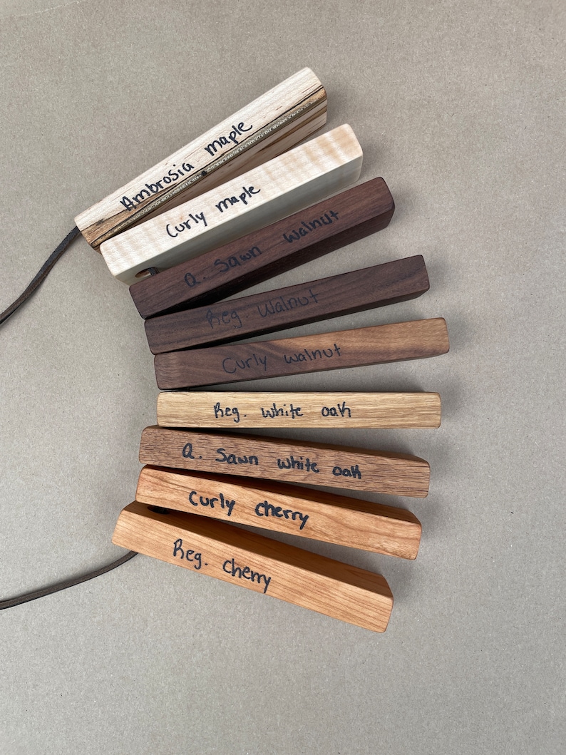 May include: A collection of wood samples labeled with different types of wood, including ambrosia maple, curly maple, walnut, white oak, and cherry.