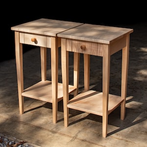 May include: Two wooden end tables with a single drawer and a lower shelf. The tables are made of light wood with a natural finish.