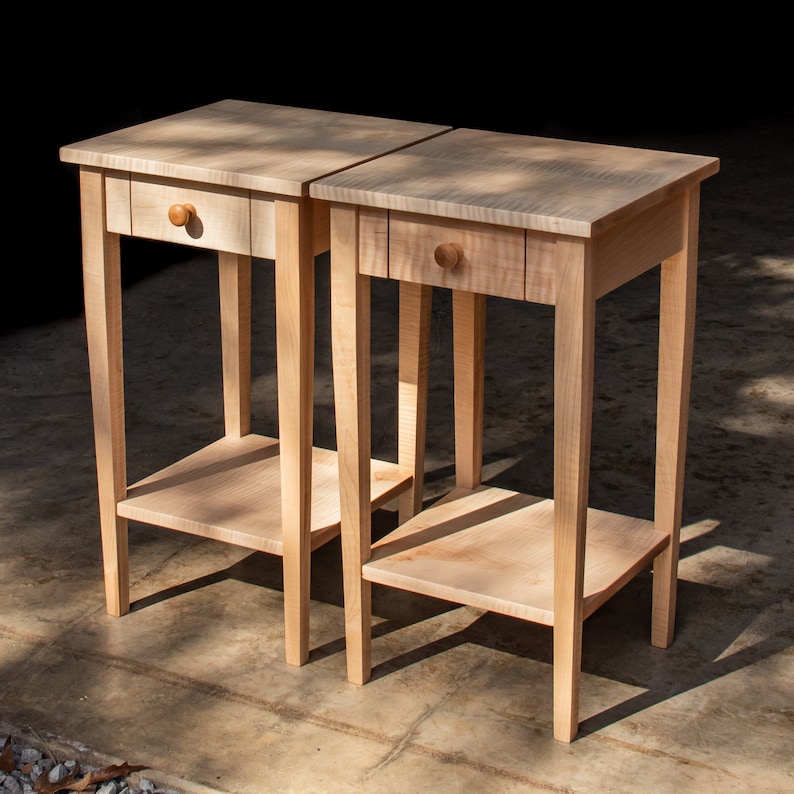 May include: Two wooden end tables with a single drawer and a lower shelf. The tables are made of light wood with a natural finish.