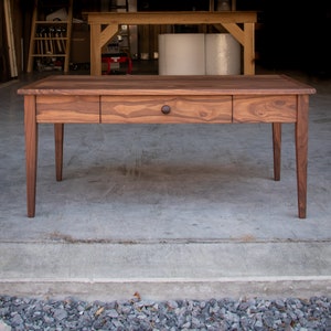 May include: A wooden table with a single drawer and a dark brown finish. The table has four legs and a rectangular top.