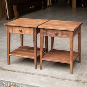 May include: Two wooden end tables with a drawer and a lower shelf. The tables are made of dark wood and have a simple, traditional design.