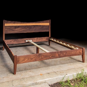 May include: A wooden bed frame with a curved headboard and a slatted base. The frame is made of walnut wood and has a natural finish.