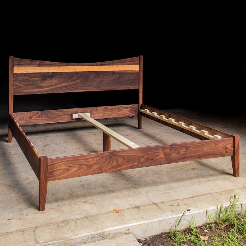May include: A wooden bed frame with a curved headboard and a slatted base. The frame is made of walnut wood and has a natural finish.