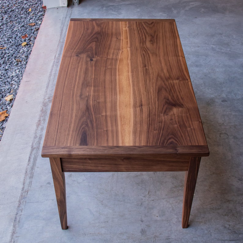 May include: A dark brown wooden coffee table with a rectangular top and four legs. The table top has a natural wood grain pattern.