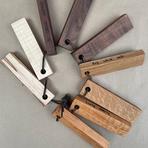 May include: A collection of eight wooden bottle stoppers, each with a different type of wood. The wood types are labeled: "0-Dawn-Walnut", "Curly Cherry", "Fig. White Oak", and "Walnut".