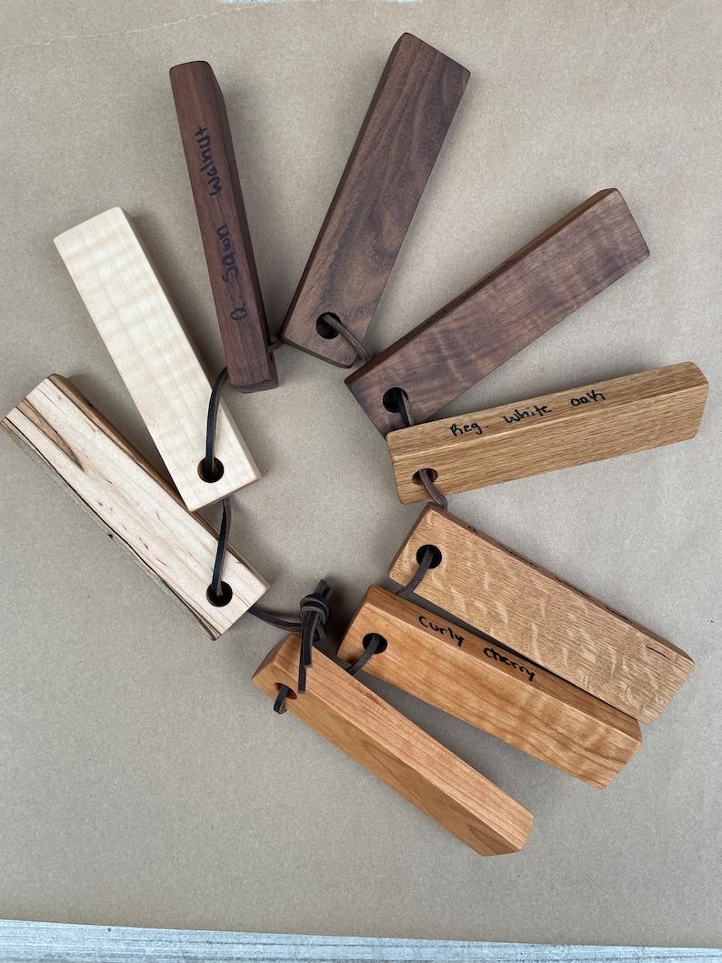 May include: A collection of eight wooden bottle stoppers, each with a different type of wood. The wood types are labeled: "0-Dawn-Walnut", "Curly Cherry", "Fig. White Oak", and "Walnut".