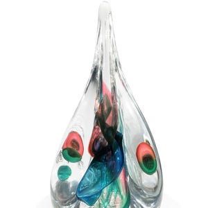 May include: Clear glass art sculpture in a teardrop shape. The sculpture contains colorful swirls of blue, pink, and green glass. The piece has a smooth, polished finish and sits on a white base. A decorative art piece.