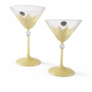 May include: Two martini glasses with a pale yellow stem and base. The clear glass bowl has a yellow floral design. A clear crystal bead is on the stem. The glasses are on a white background.