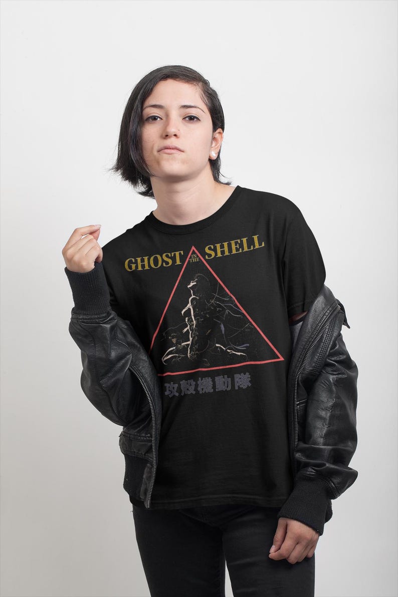 May include: Black t-shirt featuring the text "GHOST IN THE SHELL" in gold lettering above a red triangle graphic. The graphic includes a silhouette of a figure. Below the triangle is Japanese text.