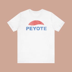 Op de afbeelding: Wit T-shirt met een verweerd rood halve cirkel ontwerp boven het woord "PEYOTE" in blauw. De afbeelding heeft een vintage stijl. Het shirt is gemaakt van een zacht materiaal en heeft korte mouwen.