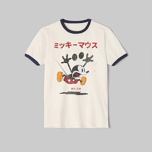 May include: A cream-colored ringer t-shirt with dark blue trim on the collar and sleeves. The front features a distressed black and red graphic of Mickey Mouse with his arms raised, accompanied by the Japanese text "ミッキーマウス" and "東京、日本".