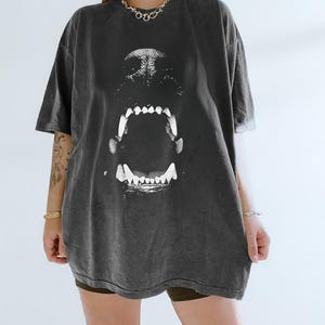 May include: Dark grey oversized t-shirt with a large graphic of a dog's open mouth and teeth. The shirt has a vintage, washed appearance and short sleeves. The design is centred on the front of the tee.