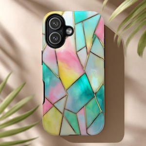 May include: A colorful phone case with a geometric stained glass design. The case features a mix of pink, yellow, teal, and white colors, outlined with gold-colored lines. The phone case has a dual-lens camera cutout.