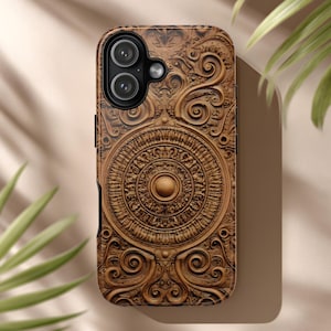 May include: A brown phone case with an intricate, carved design. The case features a central circular pattern with detailed scrollwork and a raised, textured surface. The phone's camera lenses are visible at the top.