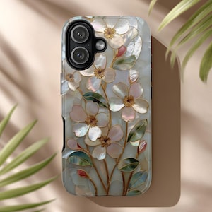 May include: A phone case featuring a floral design with white, pink, and gold accents. The case has a pearlescent background and a detailed relief of flowers and leaves. The design includes a camera cutout and black edges.