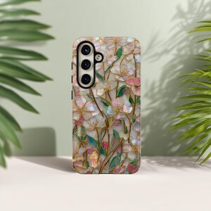 May include: A mobile phone case featuring an iridescent, mother-of-pearl style floral pattern with pink and white petals, green leaves, and thin gold outlines. The case has a black camera module cutout with three circular lens openings on the left.