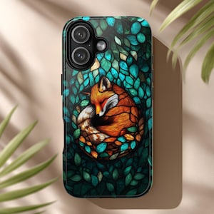 Puede incluir: Funda de teléfono con un diseño de zorro durmiente. El zorro es de color naranja y blanco, acurrucado entre hojas verdes y turquesas. La funda tiene un acabado brillante y un borde negro.