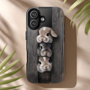 May include: A phone case featuring three adorable bunnies peeking through a wooden fence. The bunnies have soft, fluffy fur in shades of brown and gray. The case is black with a glossy finish, and the design is a charming, whimsical touch.