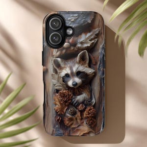 Op de afbeelding: Telefoonhoesje met een gedetailleerd 3D-reliëf van een wasbeer te midden van herfstbladeren en dennenappels. De hoes heeft een houtnerftextuur en een donkere rand.