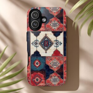 May include: A phone case with a colorful, patterned design reminiscent of a Persian rug. The case features a mix of red, blue, and cream colors in a geometric arrangement. The case has a camera cutout.