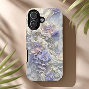 May include: A phone case with a white marble effect, adorned with a sculpted relief of a woman and lavender and pink flowers. The case has a black camera section and a glossy finish.