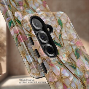 May include: A protective phone case featuring an iridescent mother-of-pearl floral pattern with gold-toned outlines. The case has a black camera cutout housing three lenses and black side buttons. Text on the image reads: Raised edges protect screen & camera.