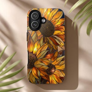 Pode incluir: Uma capa de telemóvel com um design de girassol em vitral. A capa tem um acabamento brilhante e apresenta um arranjo vibrante de pétalas amarelas, laranja e castanhas. O design inclui a câmara e o flash do telemóvel.