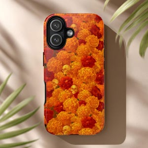 May include: A phone case featuring a vibrant floral design with orange and red marigolds and small skull accents. The case has a black border and camera cutouts, offering a unique and artistic aesthetic.