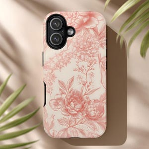 Könnte beinhalten: Eine Handyhülle mit einem floralen Muster aus rosa Pfingstrosen auf cremefarbenem Hintergrund. Die Hülle hat einen schwarzen Rand und Aussparungen für Kamera und Knöpfe. Das Design ist elegant und feminin.