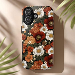 May include: A phone case with a floral design. The case features a dark background with white daisies, red poppies, and orange and yellow flowers. The case has a glossy finish and a camera cutout.