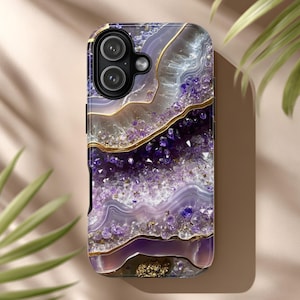 May include: A smartphone case with a purple and gold geode design. The case features a layered pattern with shades of purple, white, and gold. The design has a textured appearance, with a glossy finish. The camera lenses are visible at the top.