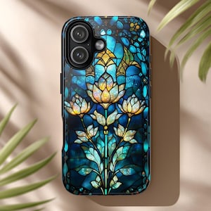 Puede incluir: Funda de teléfono con un diseño de vidriera con un motivo floral en tonos azules, turquesas y dorados. La funda tiene un acabado brillante y un borde oscuro. Las lentes de la cámara son visibles en la parte superior.