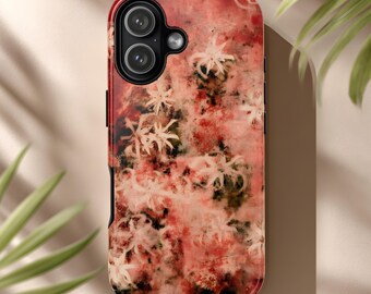 Puede incluir: Una funda de teléfono con un diseño floral en tonos rojos, rosas y blancos. La funda tiene un acabado brillante y un borde negro. Las lentes de la cámara son visibles en la parte superior.
