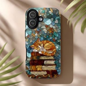 May include: A phone case featuring a sleeping orange tabby cat atop a stack of books. The case has a stained-glass design with blue, green, and brown hues. The cat is curled up, with its eyes closed, resting on the books.