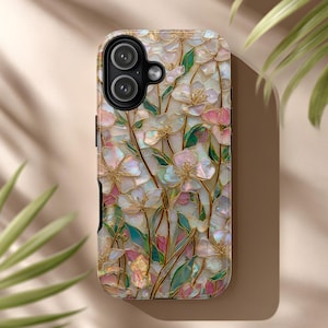 Op de afbeelding: Een telefoonhoesje met een bloemenontwerp. Het heeft witte, roze en gouden bloemen met groene bladeren. De hoes heeft een glanzende afwerking en een uitsparing voor een dubbele camera.