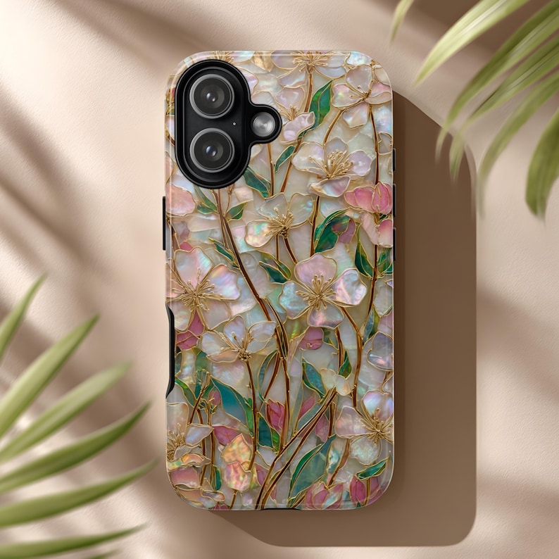 May include: A smartphone case featuring an iridescent, mother-of-pearl style floral pattern with pink and white petals, green leaves, and gold-toned stems. The design covers the entire back surface, including a cutout for a dual-lens camera system.
