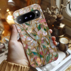 May include: A rectangular smartphone case featuring an iridescent, mother-of-pearl style floral pattern. The design displays pink and white flower petals with green leaves and gold-toned outlines, creating a stained-glass effect across the surface.