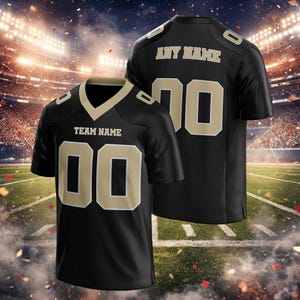 Puede incluir: Camiseta de f&uacute;tbol negra con detalles dorados. La camiseta muestra "TEAM NAME" y el n&uacute;mero "00" en la parte delantera. La parte trasera muestra "ANY NAME" y el n&uacute;mero "70". La imagen muestra la camiseta sobre un fondo de estadio.