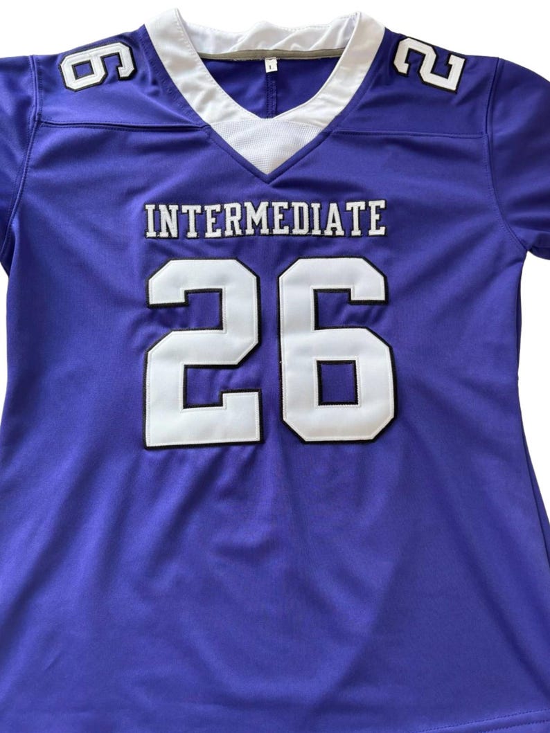 Puede incluir: Una camiseta de f&uacute;tbol morada con detalles blancos y negros. La camiseta muestra la palabra "INTERMEDIATE" y el n&uacute;mero "26" en letras blancas. El n&uacute;mero "6" est&aacute; en el hombro izquierdo y el n&uacute;mero "2" en el hombro derecho.